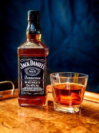 Bottle of Jack Daniel's whiskey with a glass of whiskey on a textured surface.