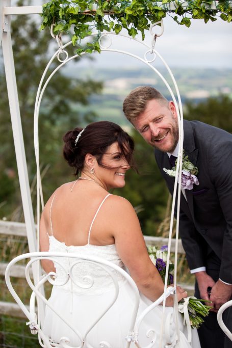 Couple posing on a swing, with lush greenery and a scenic background.