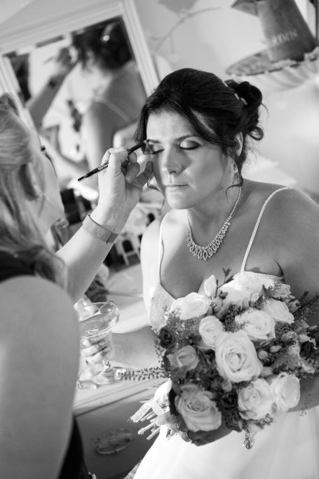 Bride getting ready with makeup applied, holding a bouquet of white and pink flowers.