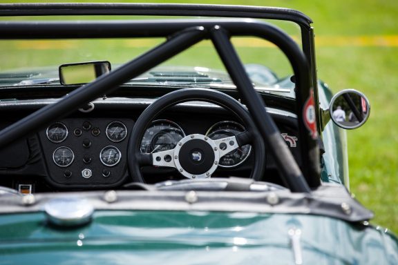 Interior of a classic sports car with a black roll bar and leather steering wheel.