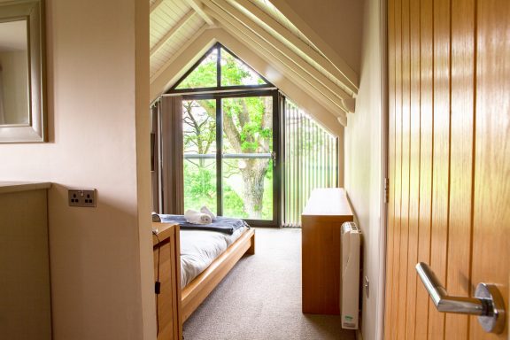 A modern bedroom with large windows overlooking greenery.