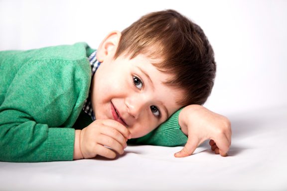 Smiling young boy in a green sweater lying on a white background.