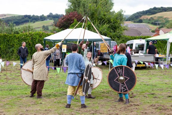 Medieval reenactors in costume, demonstrating skills with shields and props at an outdoor event.
