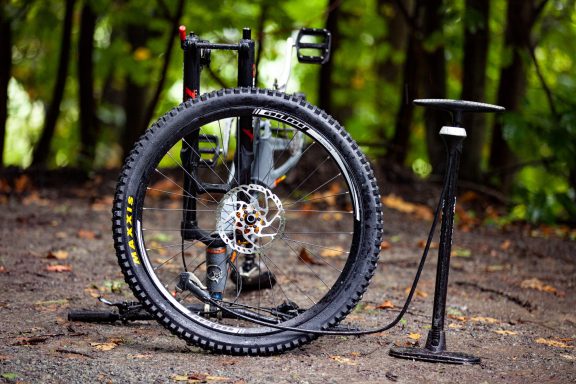 A mountain bike with a flat tyre and a pump beside it, set in a wooded area.