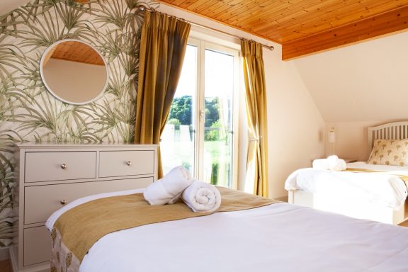 Bright bedroom featuring a double bed, dresser, and floral wallpaper.