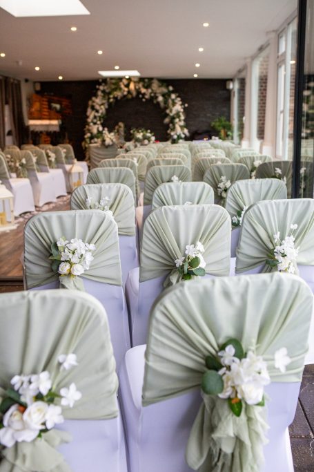 A decorated venue with rows of chairs adorned with green sashes and white floral arrangements.