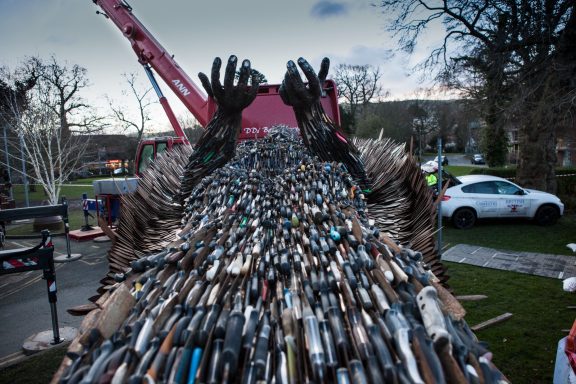 A large sculpture adorned with various knives, set in an outdoor environment.