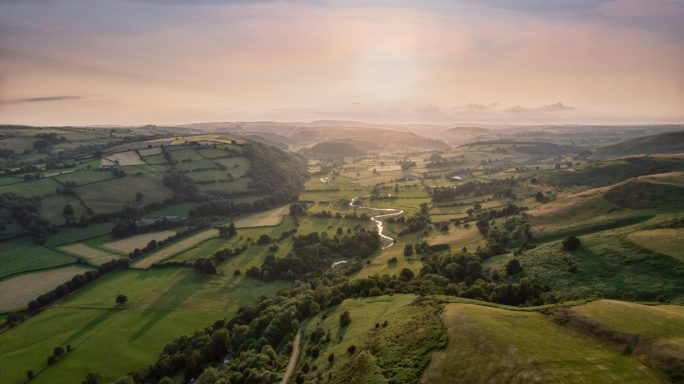 Breathtaking view of rolling green hills and a tranquil river under a vibrant sunset.
