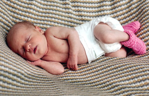 Newborn baby sleeping on a knitted blanket, wearing a diaper and pink booties.