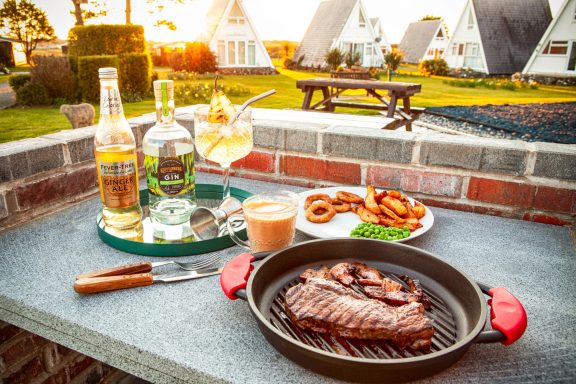Grilled steak with drinks and sides, set outdoors at a scenic holiday retreat.
