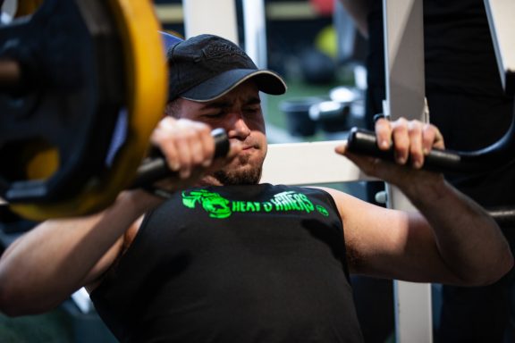 A person exercising with weightlifting equipment, focused and straining during the lift.