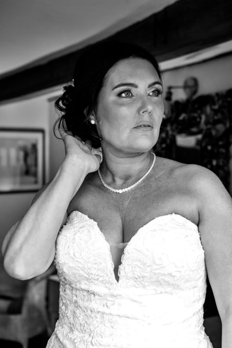 Bride adjusting her hair, wearing a strapless wedding dress and a pearl necklace.