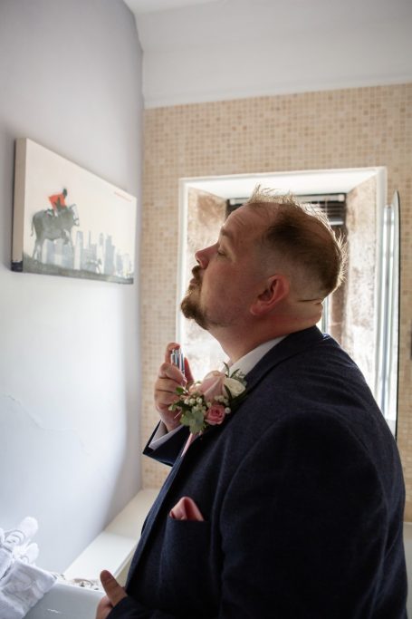 Groom spraying aftershave whilst looking up in a mirror.