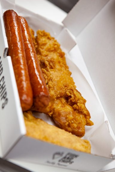 Two sausages and a piece of fried fish in a takeaway box.