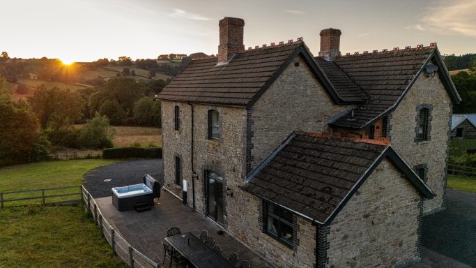 Stone cottage with a hot tub, set in a green landscape at sunset.