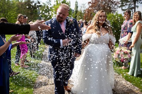 A newlywed couple walking together, surrounded by guests throwing confetti.