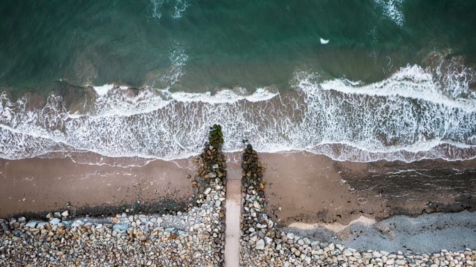 Aerial view of a sandy beach with waves lapping at the shore and a pathway leading to the water.