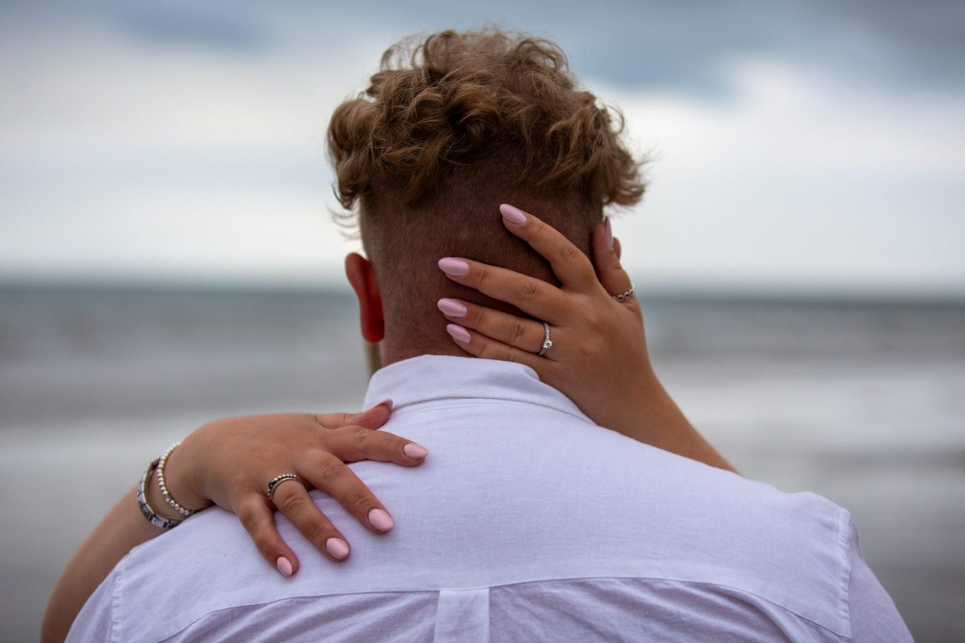 A couple embraces, with one person’s hand on the other's head, by the seaside.