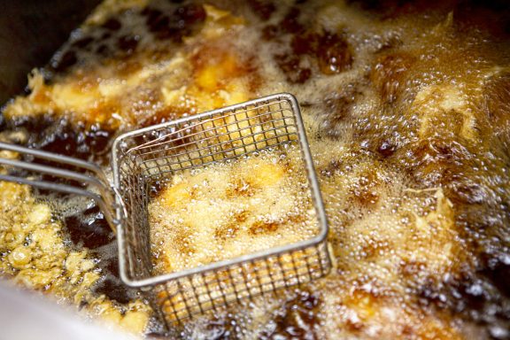 Basket partially submerged in bubbling oil with frying food.