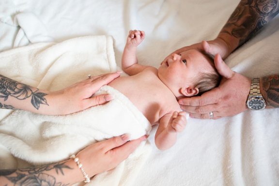 Newborn baby lying on a white blanket with hands gently supporting its head.