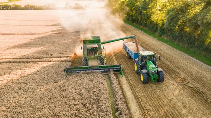 A tractor harvesting crops in a field with a trailer on a sunny day.