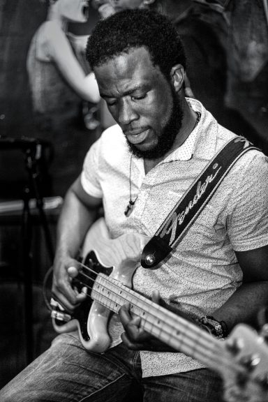 A man plays a bass guitar in a black and white setting.