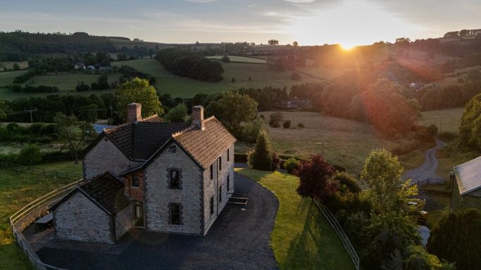 Scenic countryside view at sunset with a stone house in the foreground.