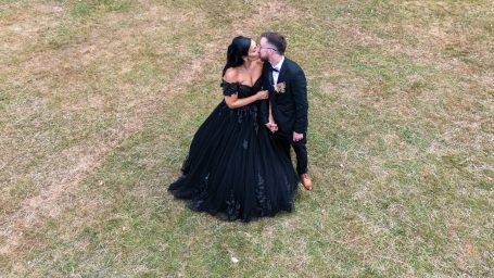 Couple in formal attire sharing a kiss on a grassy field.