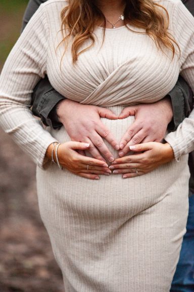 Pregnant couple's hands form a heart shape on a baby bump.