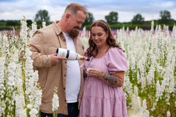 A couple in a floral field, pouring champagne and enjoying a special moment together.