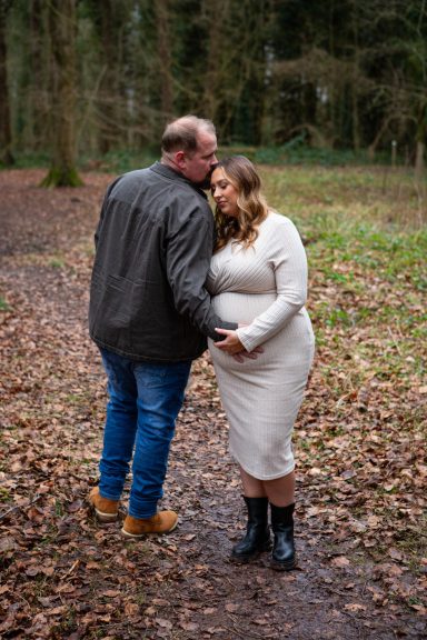 Couple embracing in a forest, with the woman showing her baby bump.