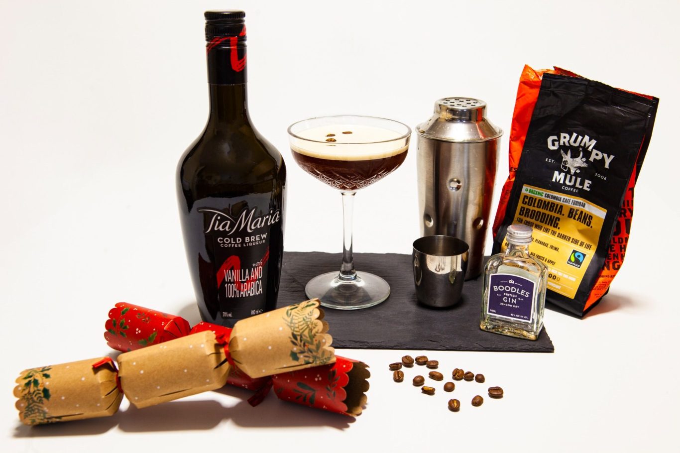 A festive display with a cocktail, bottle, coffee, and Christmas crackers.