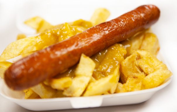 A chip shop sausage served on a bed of golden chips, drizzled with curry sauce.