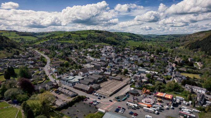 Aerial view of a quaint town surrounded by lush green hills and blue skies.