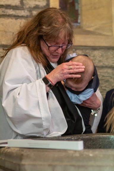 A person in a white robe gently blesses a baby held in their arms.