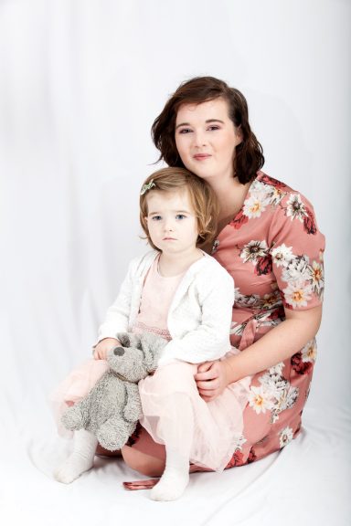 A woman and a young girl sitting together, the girl holding a grey teddy bear.