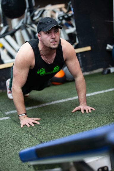 Man doing push-ups on a gym floor, wearing a black cap and tank top.