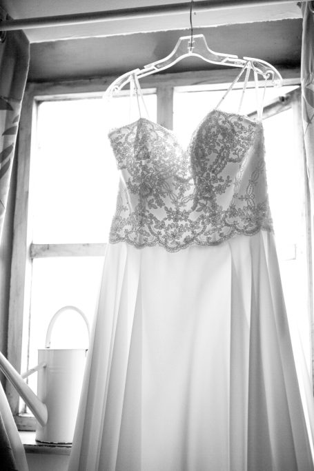 Elegant wedding dress with a beaded bodice, hanging by a window.