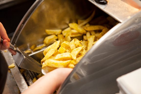 A scoop of golden fried chips being served from a fryer.