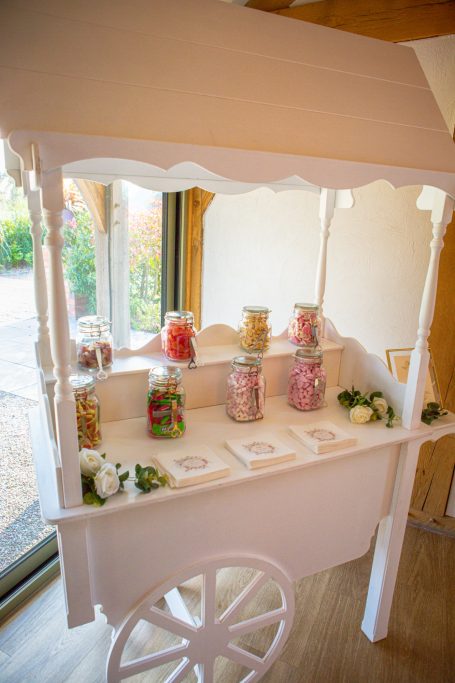 A decorative white sweet cart displaying jars of colourful candies and treats.