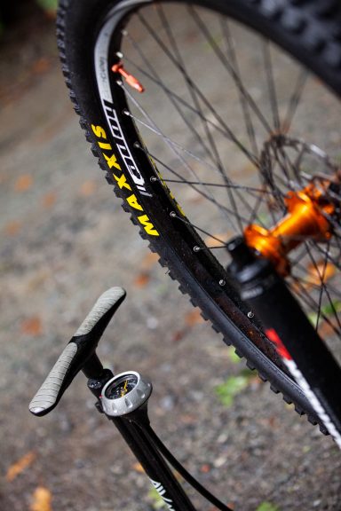 Close-up of a mountain bike wheel and a pump on gravel.