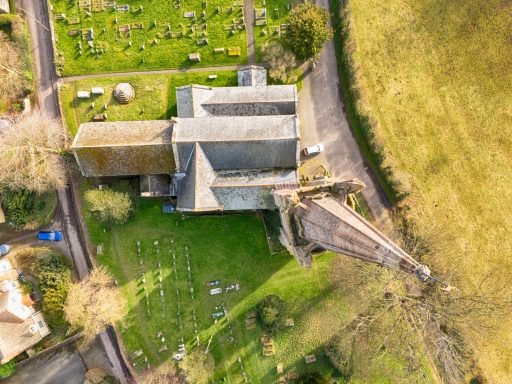 Aerial view of a church with a graveyard and surrounding greenery.