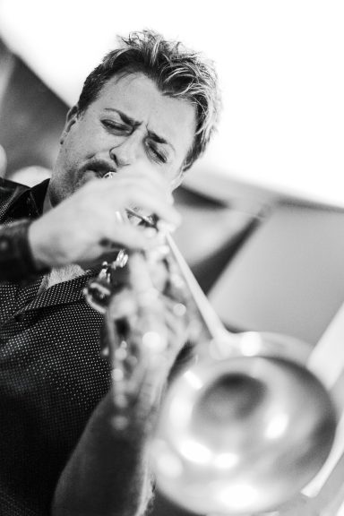 A man playing a trumpet passionately in a black and white setting.