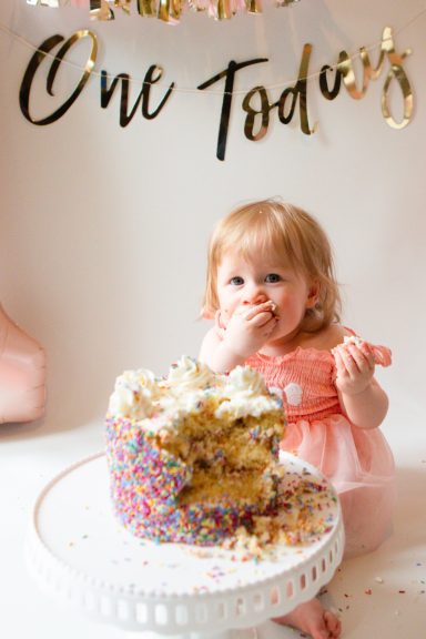 A toddler in a pink dress enjoying a large, colourful birthday cake.