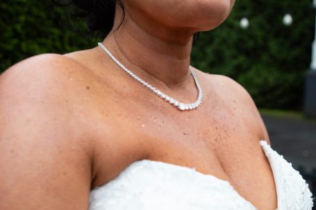 Close-up of a bare shoulder adorned with a pearl necklace against a blurred green background.