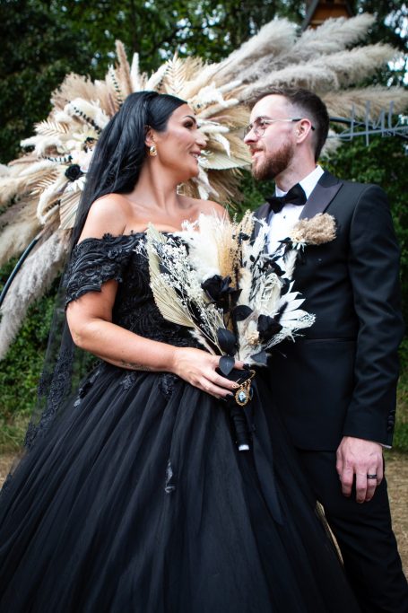 A couple in elegant attire with a dramatic black dress and a unique floral bouquet.