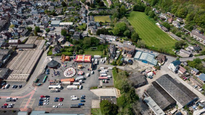 An aerial view of a town with commercial buildings, green fields, and parked vehicles.