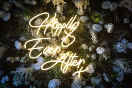 Neon sign reading "Happily Ever After" against a floral backdrop.