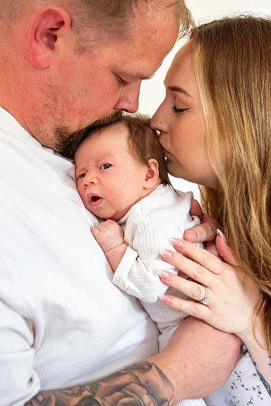 A mother and father gently hold a newborn, sharing a tender moment together.