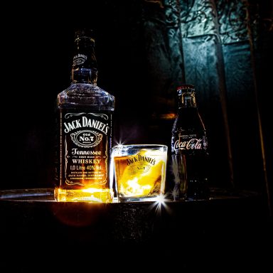 A bottle of Jack Daniel's whiskey, a glass with ice, and a Coke bottle.